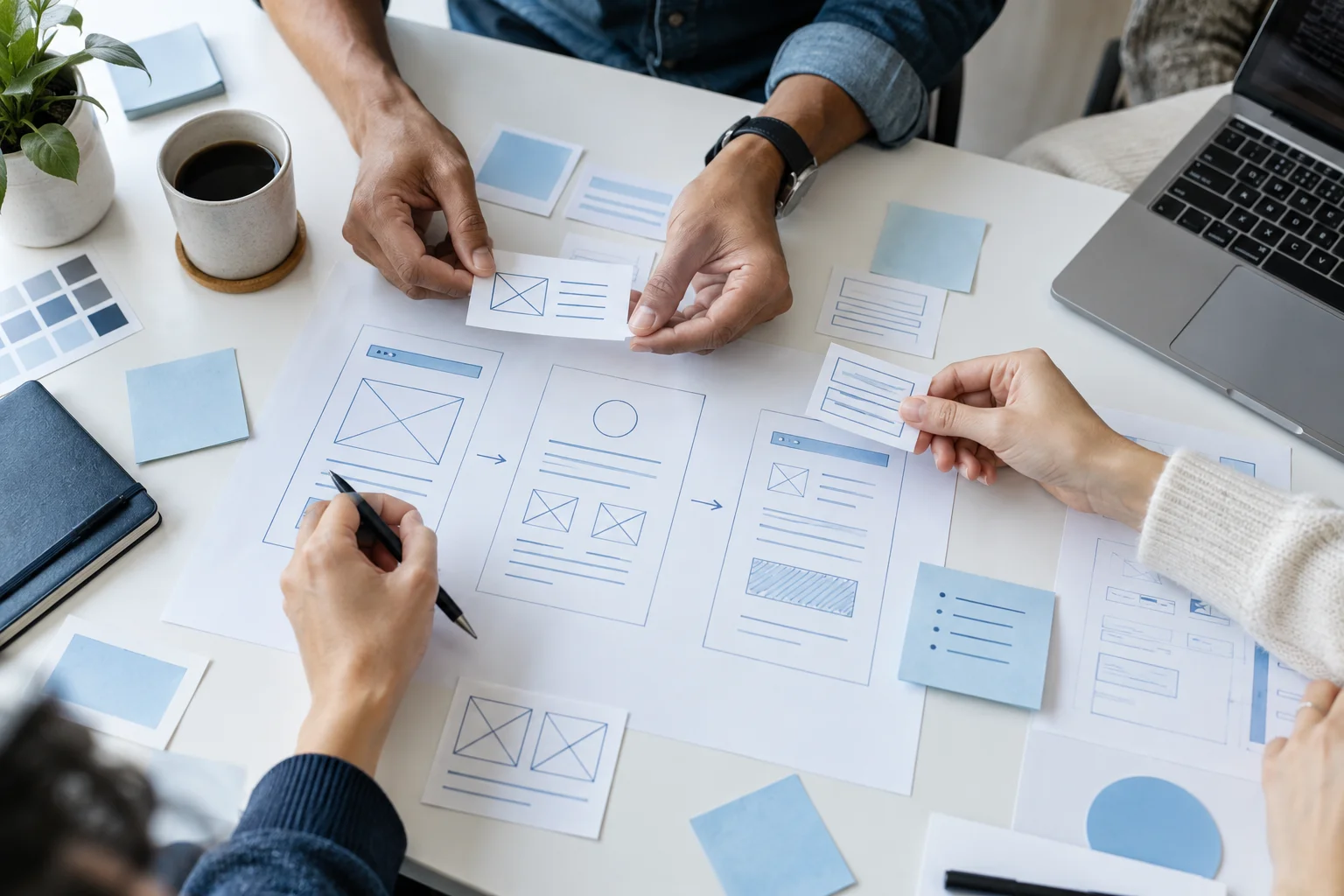 Hands arranging interface wireframes on a design desk